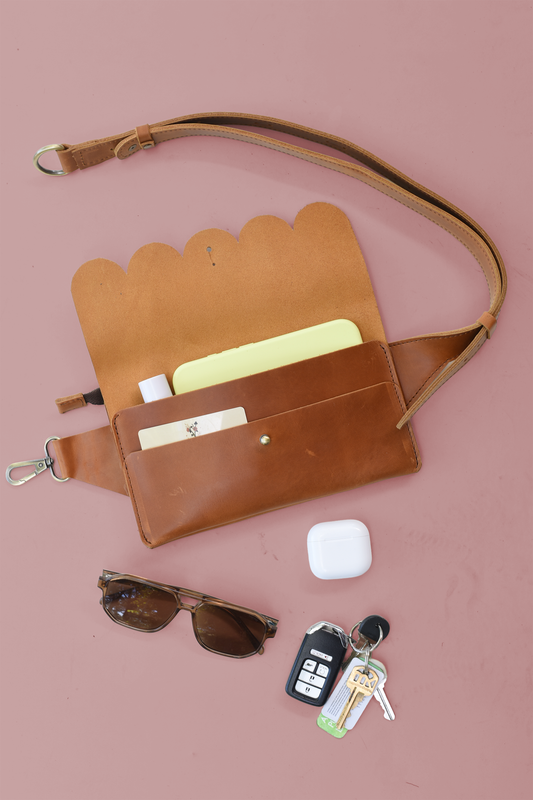 Brown leather crossbody bag with sunglasses and keys on a pink background
