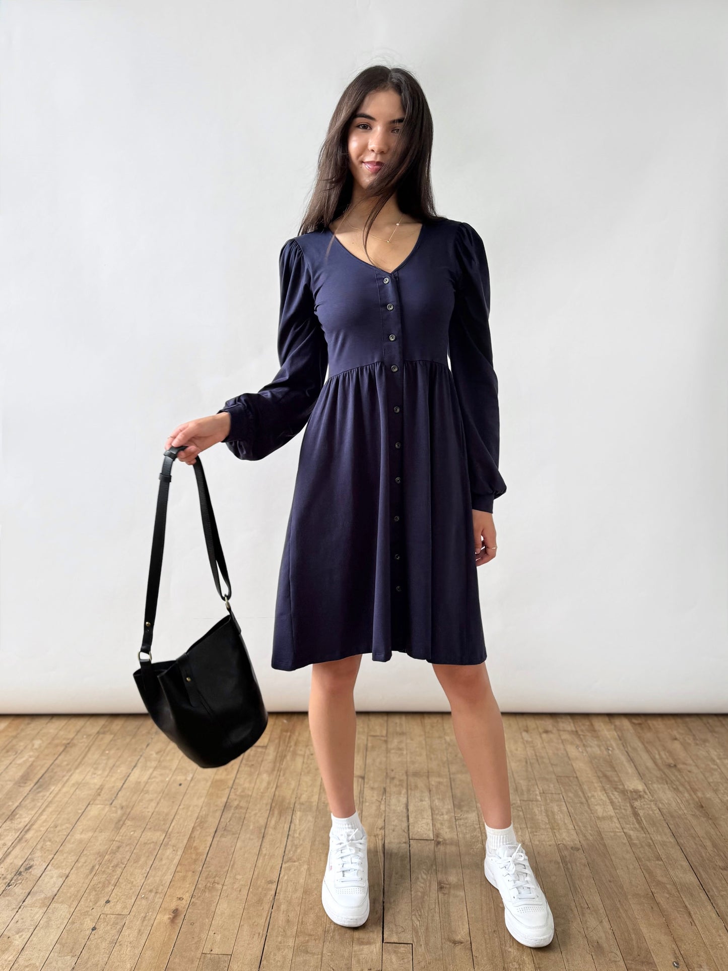 Woman wearing a dark blue dress holding a black bag indoors.