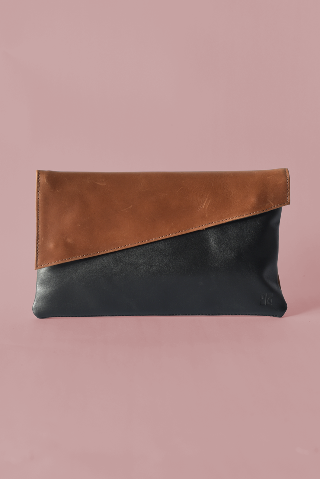 Two-tone leather clutch bag with brown top half and black bottom half on a pink background