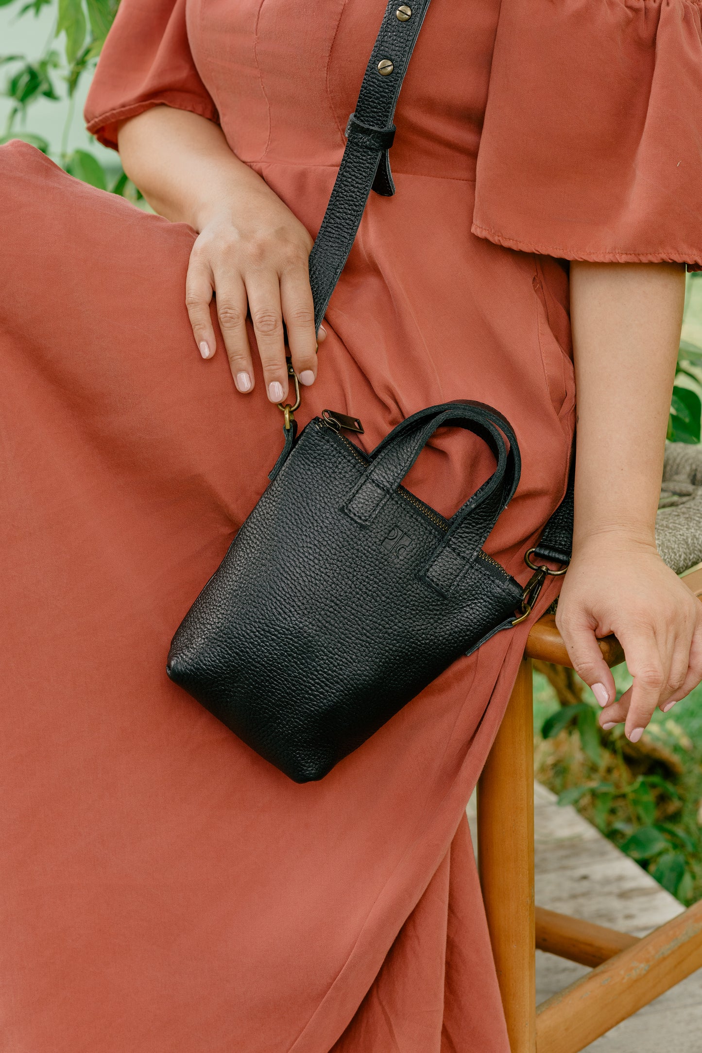 Person wearing a rust-colored dress holding a black handbag outdoors.