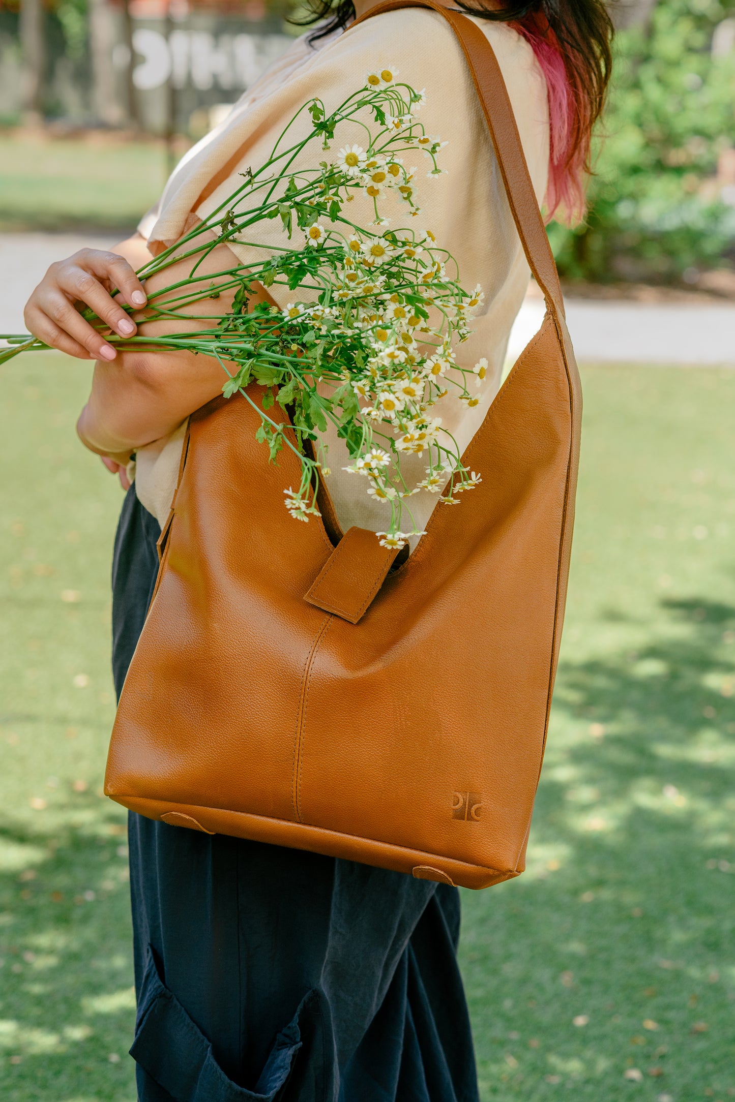 Person holding a brown leather bag with flowers, standing outdoors on grass.