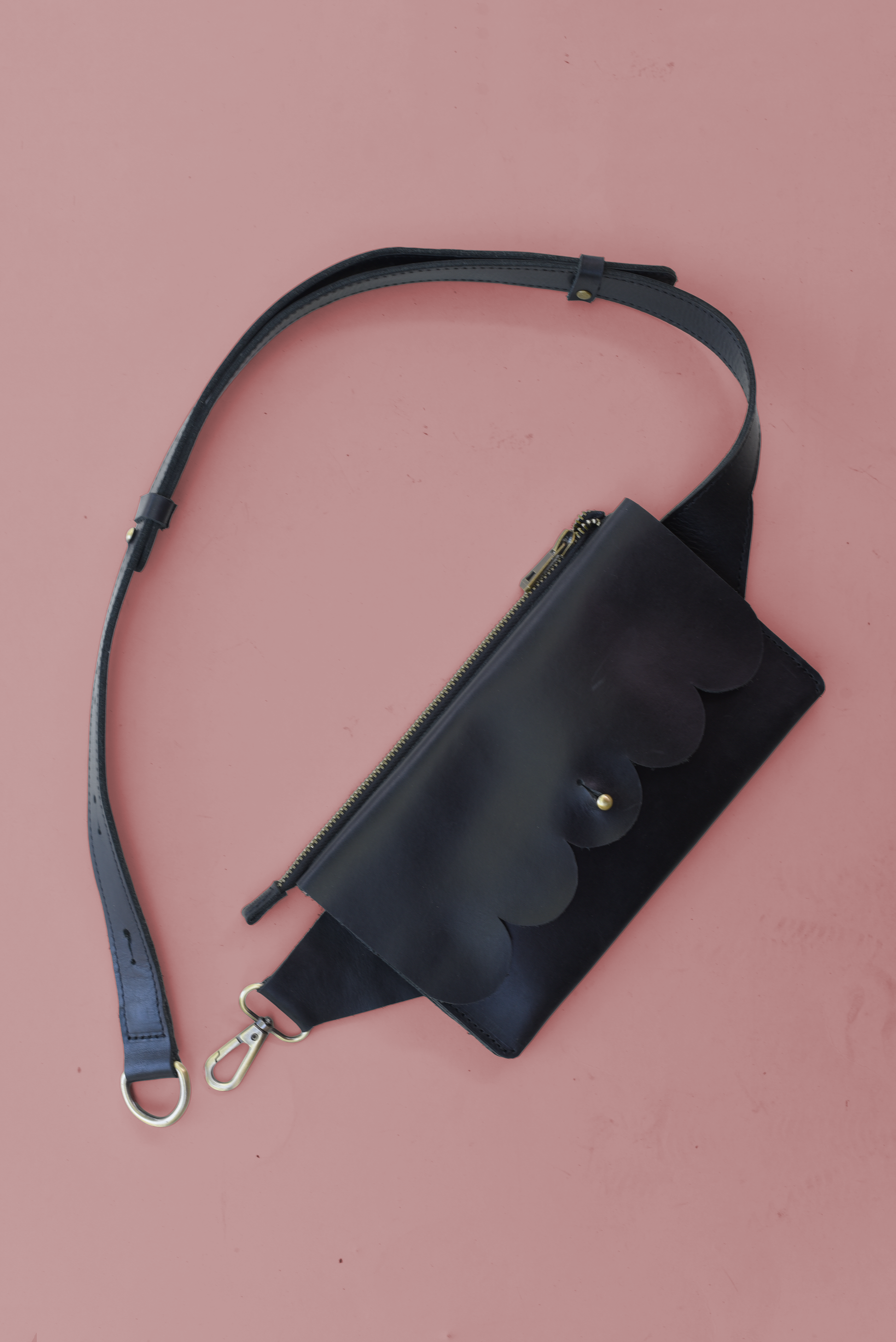 Black leather waist bag with strap on a pink background