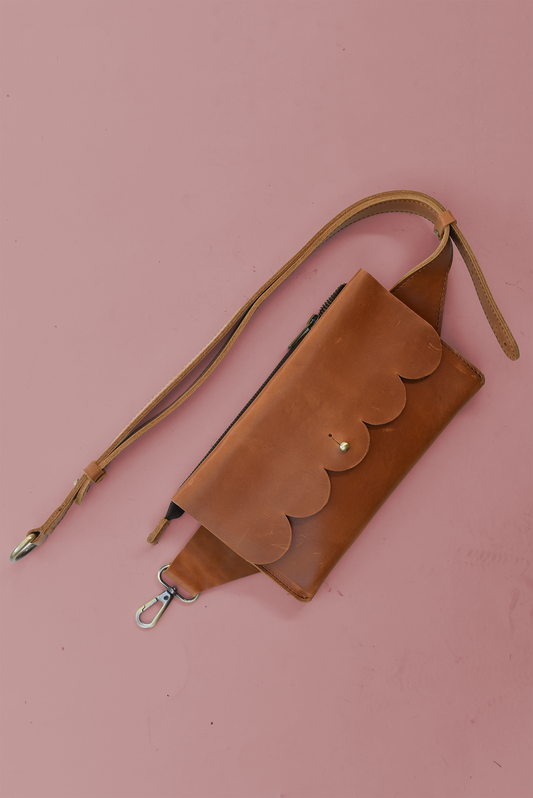 Scalloped Brown leather sling bag or fanny pack with strap on a pink background