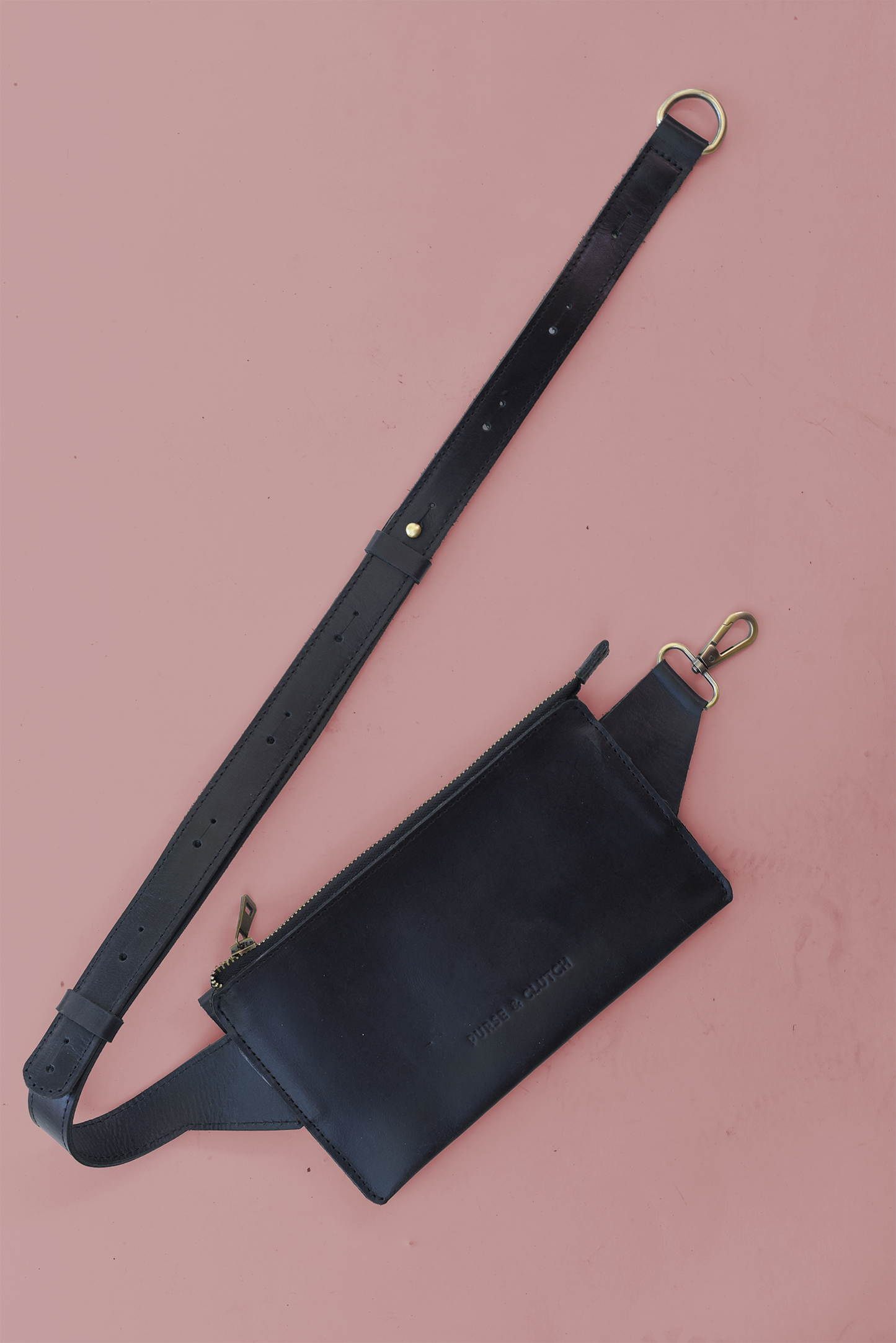 Scalloped Black leather sling bag with adjustable strap on a pink background