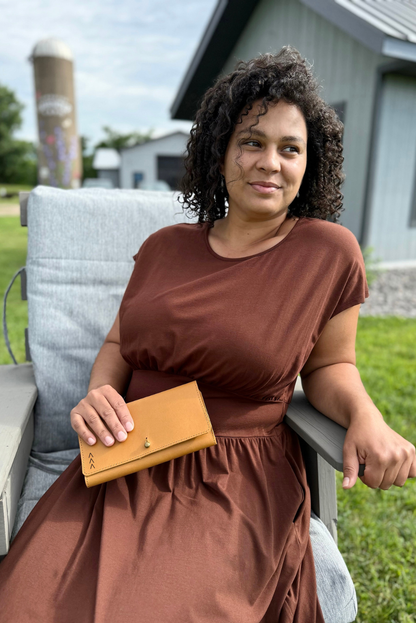 Woman in a brown dress holding a yellow clutch on a porch with a barn in the background