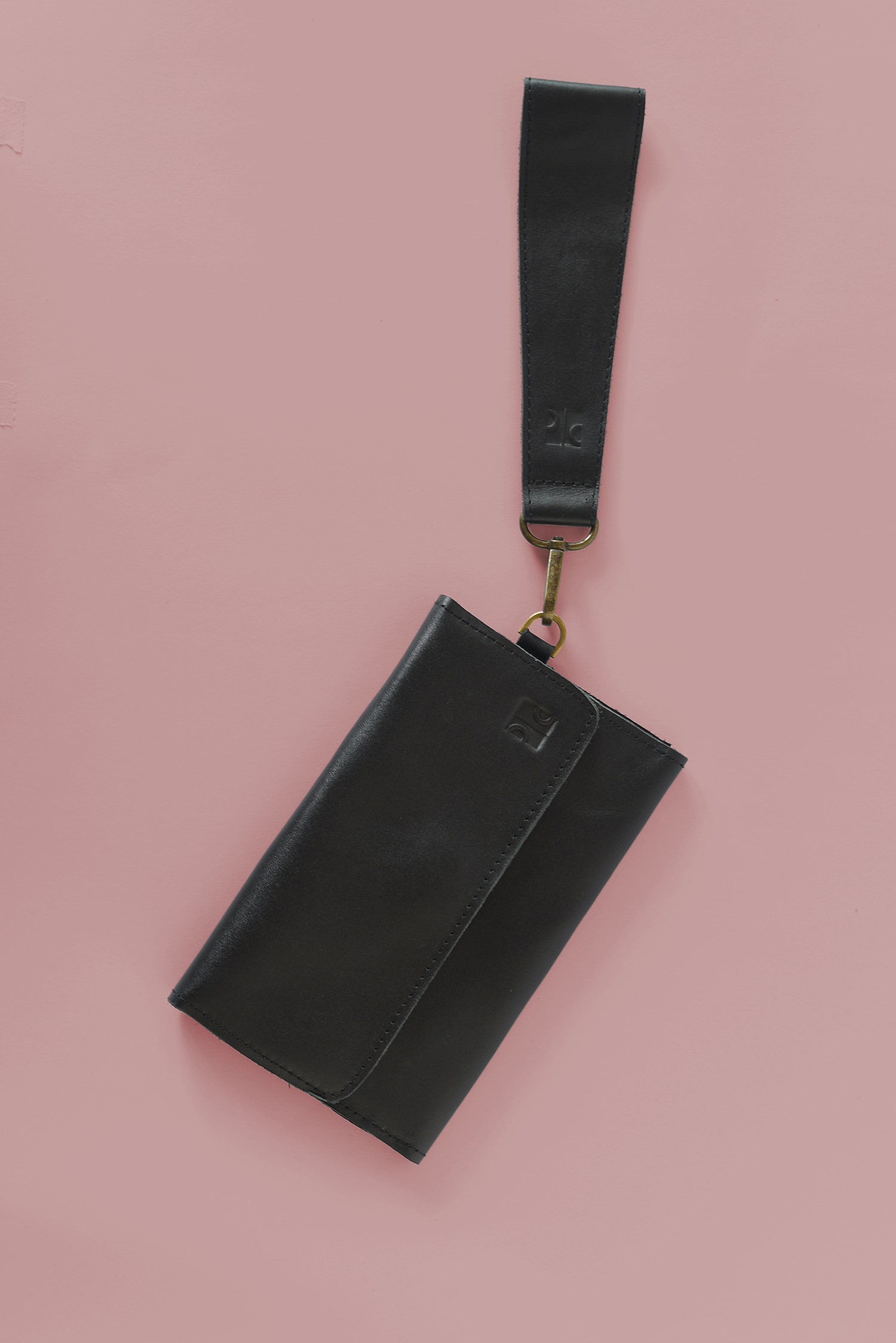 Black leather pouch with strap on a pink background