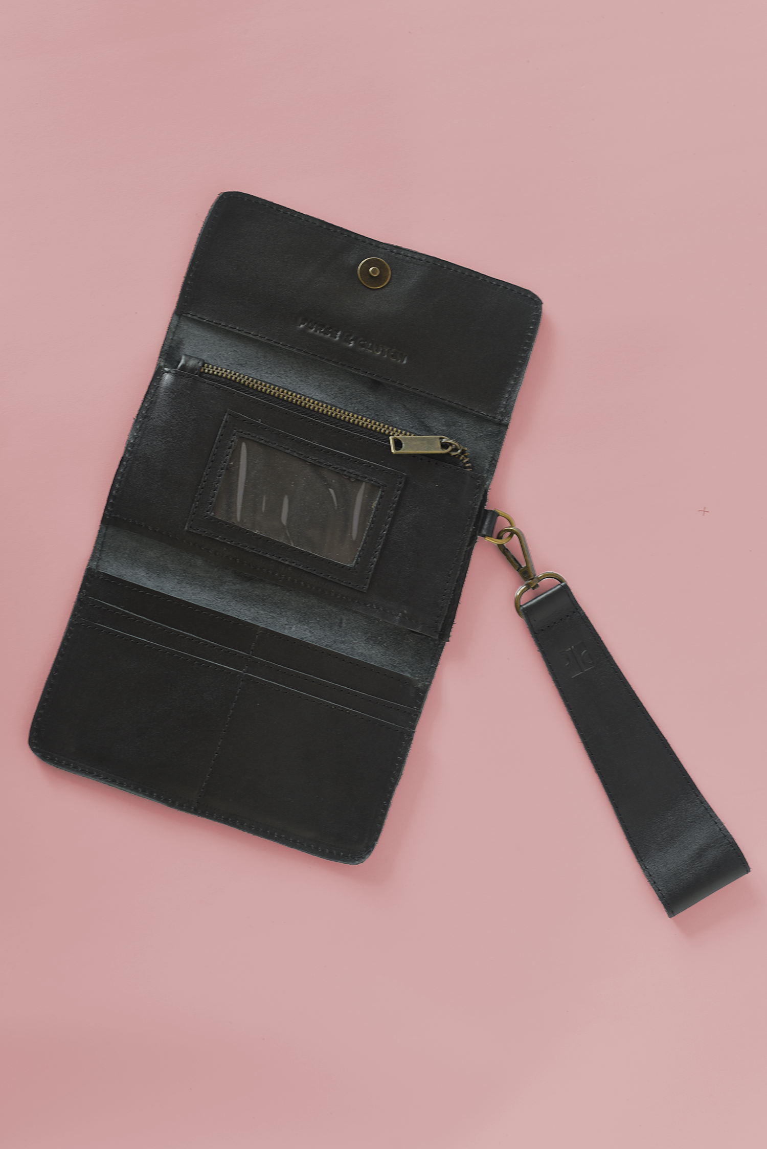 Black leather wallet with a wrist strap on a pink background